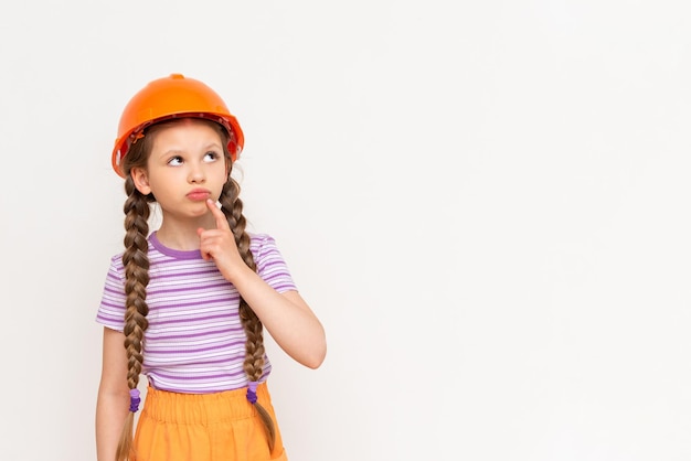 A little girl in a construction helmet looks at your advertisement on a white isolated background Copy space The concept of renovation in the children's room