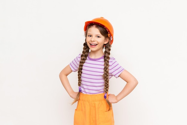 A little girl in a construction helmet and pigtails holds her hands at the waist on a white isolated background The profession of an engineer for a child