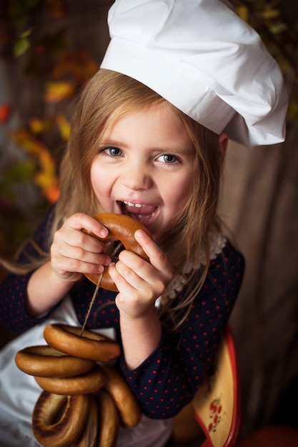 Bambina in vestiti cuoco con bagel nelle sue mani e sorridente