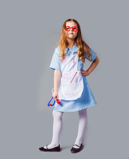 회색에 고립 된 의사 직업의 의상을 입은 어린 소녀