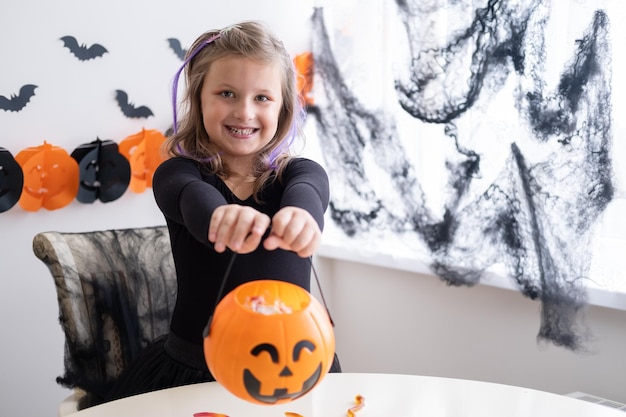 Bambina in costume di strega che tiene jack di zucca con caramelle, halloween