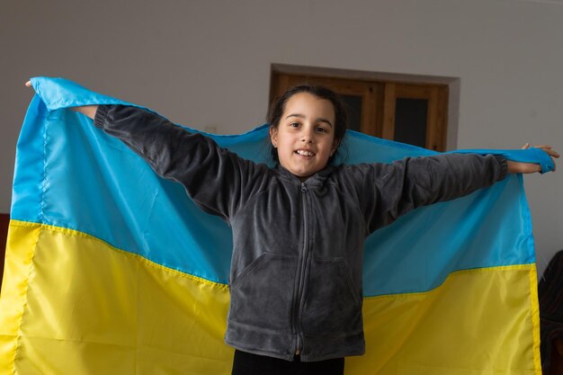little girl covered with Ukraine flag. Concept of standing with Ukrainian nation in war with Russia.