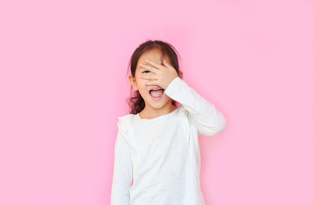 Little girl covering face and eyes by hand on pink background