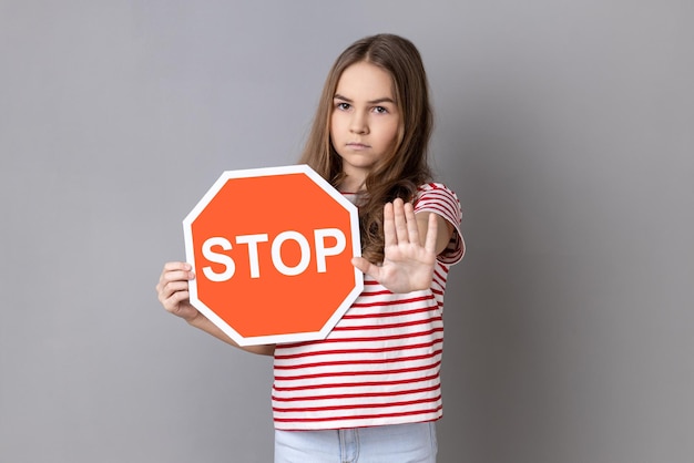 Photo little girl covering face with octagonal stop symbol showing traffic sign and ban gesture with palm