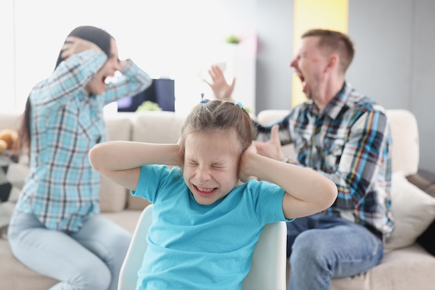 Little girl covering her ears with her hands against background of swearing parents at home