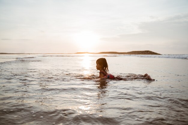 小さな女の子が水で遊んでいる間、ビーチの砂の上をクロールします。