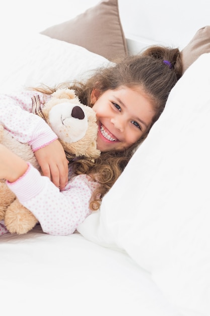 Little girl cuddling teddy bear in bed