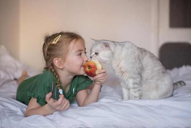 小さな女の子とかわいい猫はリンゴを食べるのが大好きです