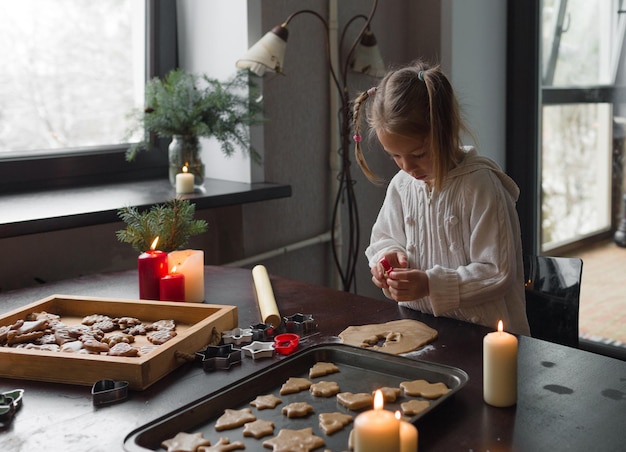 A little girl cuts out Christmas cookies from a mold