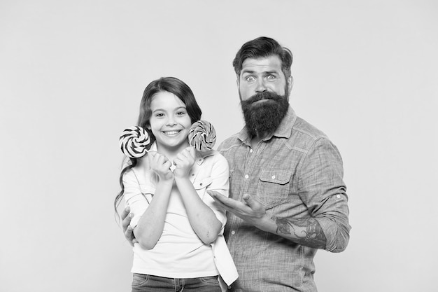 Little girl and dad hold colorful lollipop summer vibes happy family cheerful about dessert candy shop happy childhood Daughter and dad eat candy bearded hipster man is good father happiness