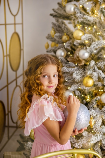 La bambina decora l'albero di natale, concetto del nuovo anno. kid vicino all'albero di natale, ragazza in abito rosa.