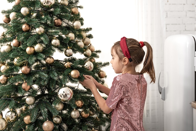 A little girl decorates a Christmas tree, hangs balls.