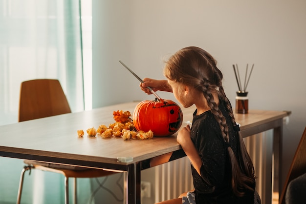 小さな女の子がハロウィーンの部屋でカボチャを飾ります。子供たちは家を飾ります。子供たちはカボチャを彫ります。不気味なハロウィーンの楽しみ