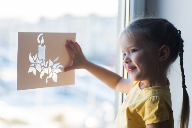 Little girl decorates the window for the new year and christmas