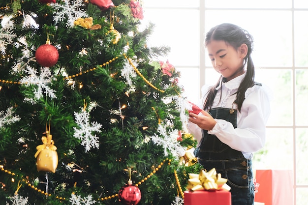 Little girl decorating Christmas tree in living room.