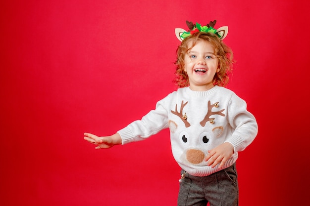 Little girl in deer horns on a red background christmas new year