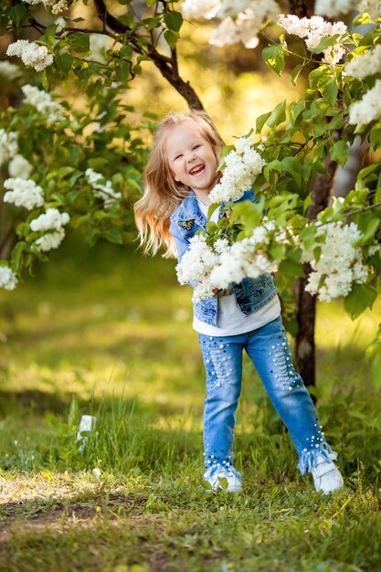 маленькая девочка в джинсовом костюме гуляет весной в сиреневом саду