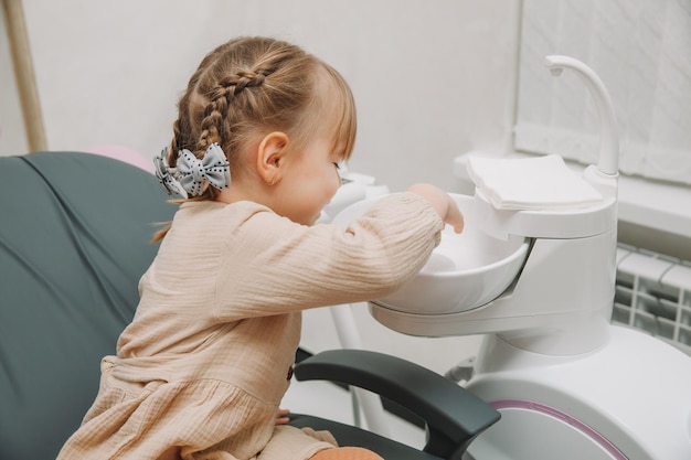 Little girl in the dentist's office spits saliva into the sink.