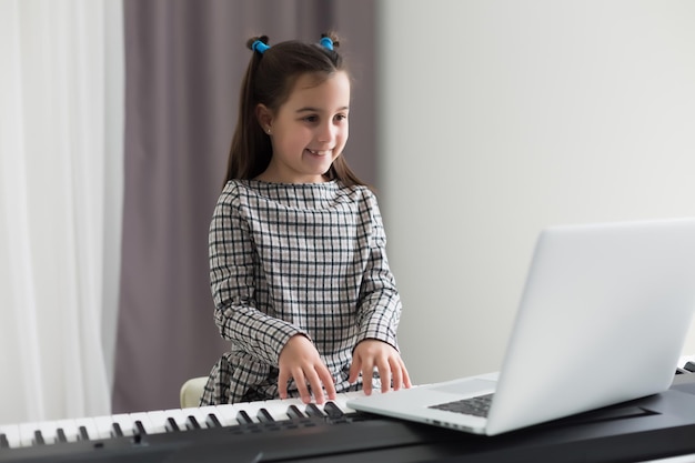 Little girl distance learning the piano online during quarantine. Coronavirus concept.