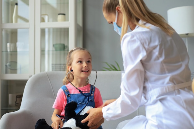 Little girl at the doctor for a checkup. Doctor playfully checking the heart beat of a teddy bear.