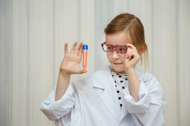 Little girl in a doctor s smock examines test tubes with tests.