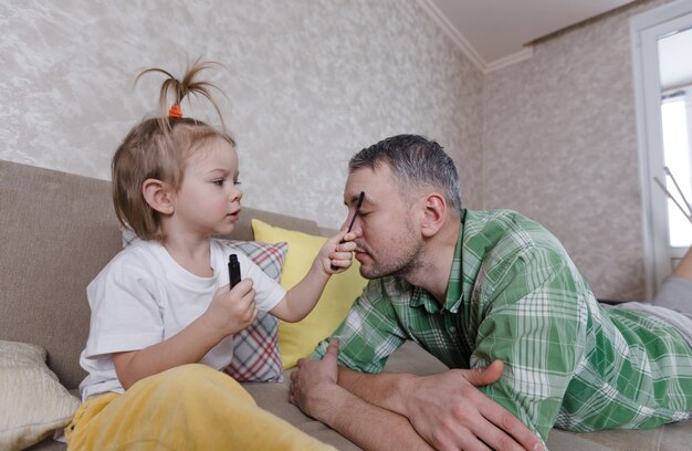 A little girl does makeup to her father during games together