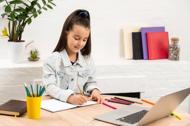 Little girl doing her homework at home and using a laptop