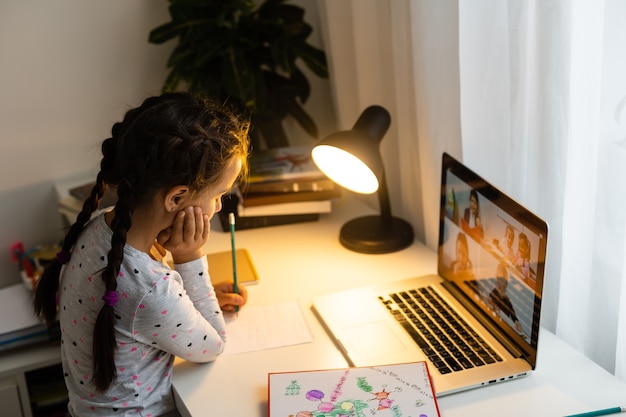 Little girl doing her homework at home and using a laptop