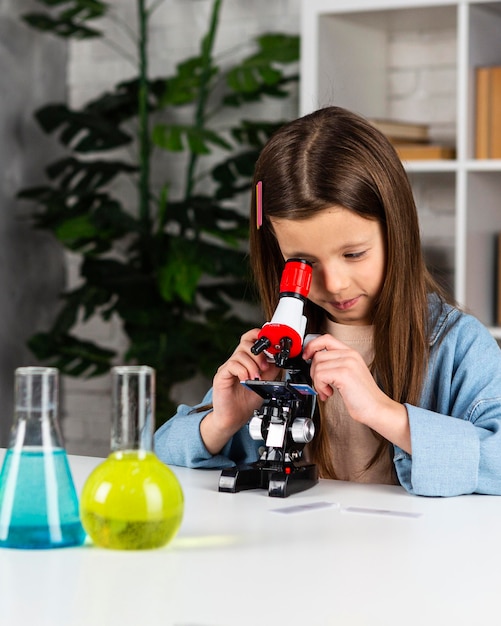Фото Маленькая девочка делает научные эксперименты и смотрит в микроскоп