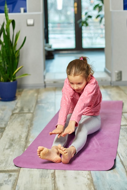 Bambina che fa esercizi di stretching, pratica yoga sul tappetino fitness a casa