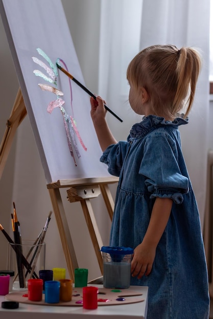 little girl drawing a picture on canvas on an easel