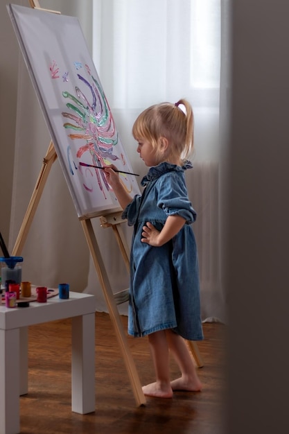 little girl drawing a picture on canvas on an easel