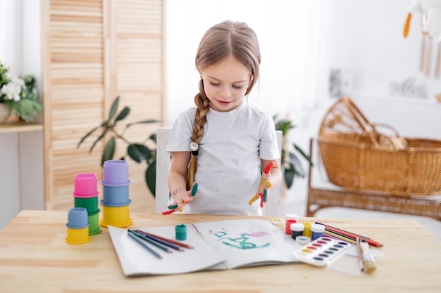 a little girl draws drawings with multicolored paints or learns to draw in a bright children's room at home or in kindergarten a smiling child the lifestyle of a preschooler child