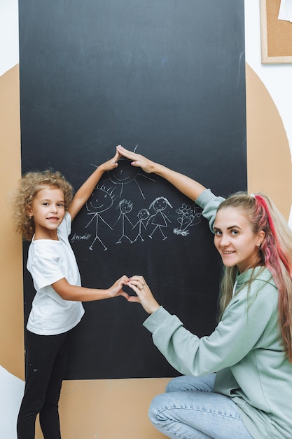 Photo little girl draws a family on a chalkboard