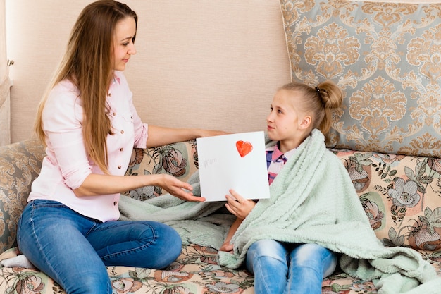 A little girl draws a greeting card for mom on mother's day with the words "I love you, mom." girl shows mom drawing with a heart