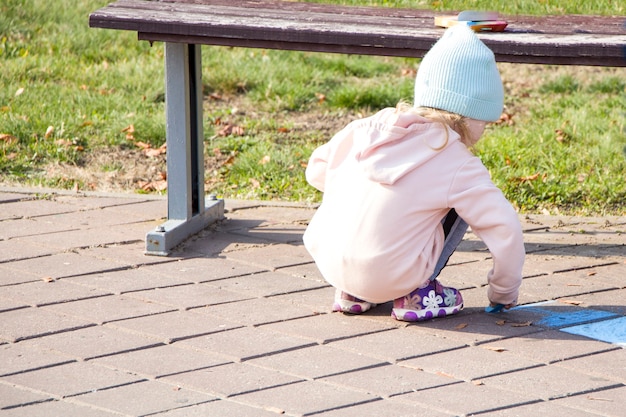 Little girl draws with chalk. The park. Autumn.