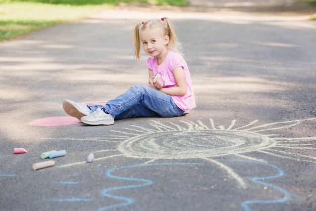 Little girl draws with chalk on pavement