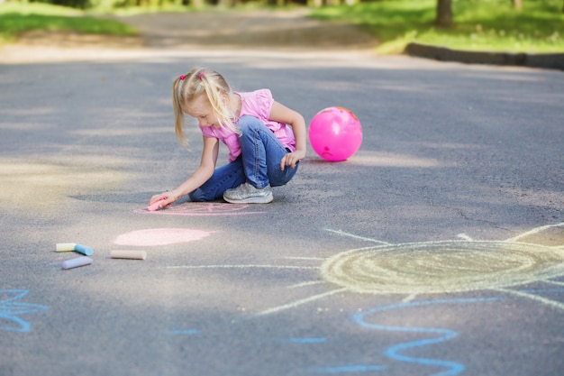 Little girl draws with chalk on  pavement