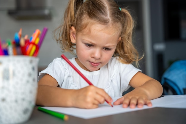 Маленькая девочка рисует цветными карандашами дома.
