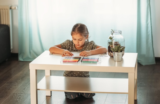 A little girl draws with colorful markers in the room