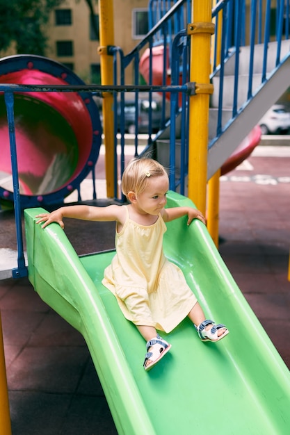 Little girl in a dress slides down a slide on the playground