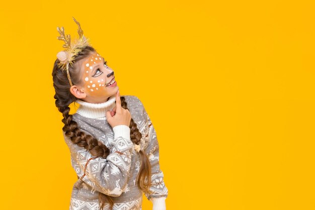 A little girl dressed as a christmas reindeer looks at your advertisement and smiles new years carnival for children yellow isolated background copy space