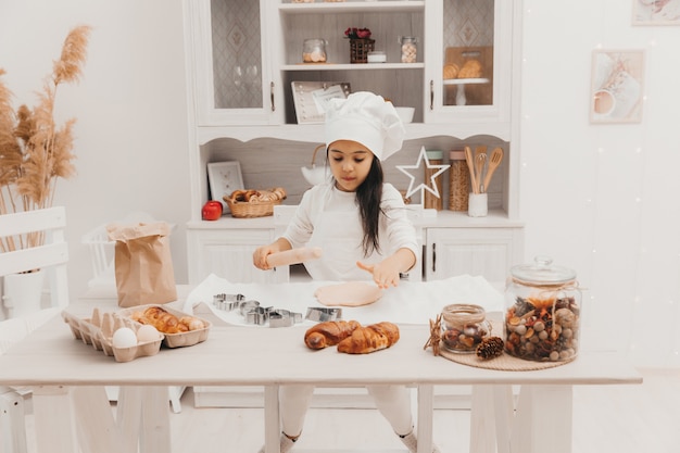 A little girl dressed as a cook in the kitchen prepares cookies.