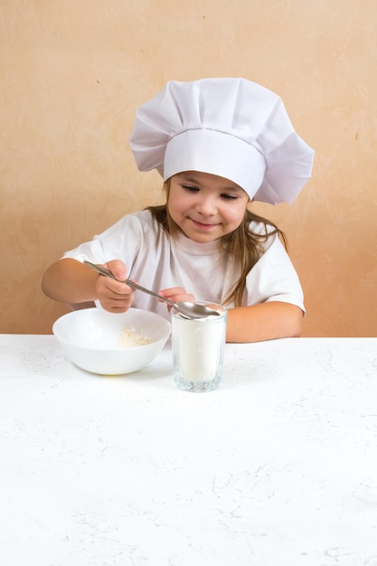 Маленькая девочка, одетая как повар, замешивает тесто, готовит концепцию детского образа жизни. Ребенок любит весело учиться и играть на кухне.