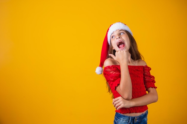 Little girl dressed for christmas pointing with her thumb on free space for text. year-end promotion and campaigns