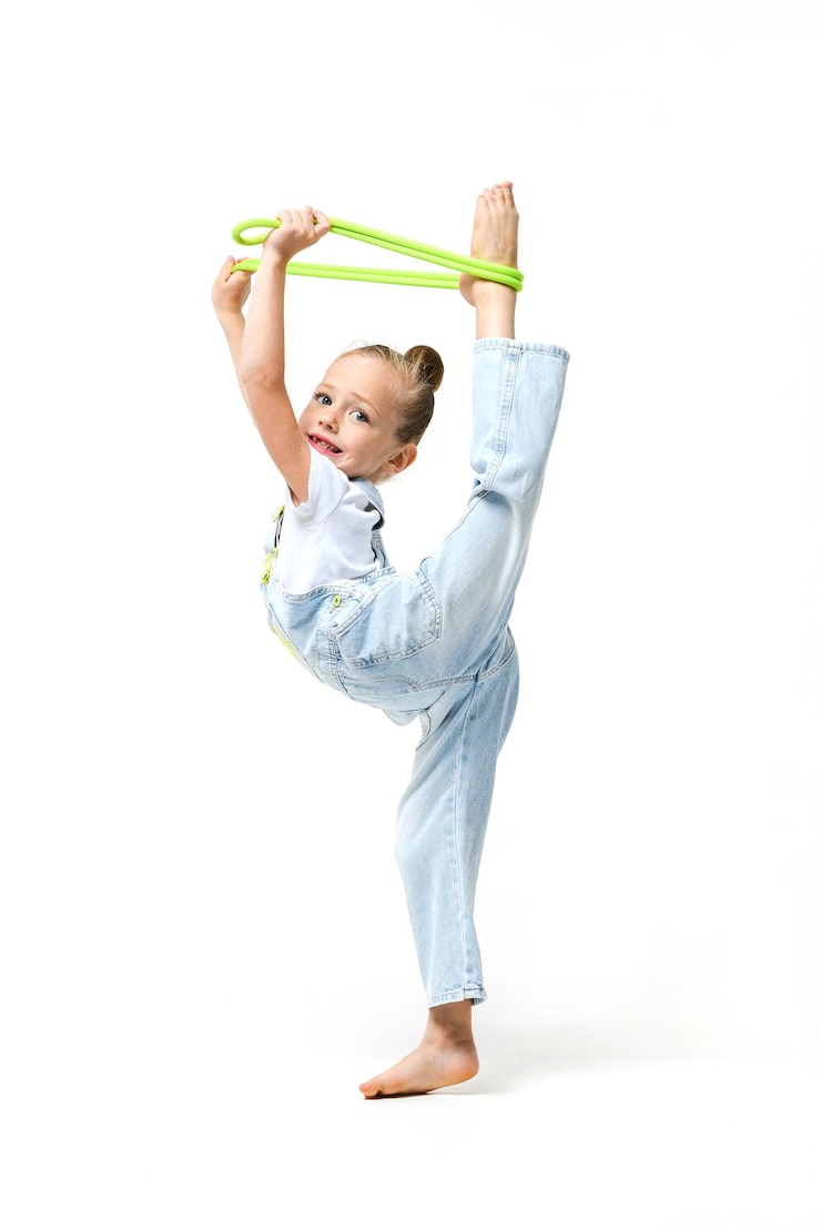 Photo little girl dressed in denim overalls put feet on head with jumping rope