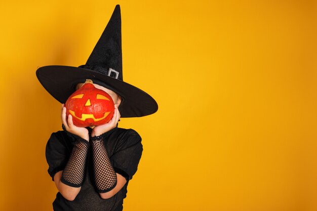 Little girl dressed in a witch costume holds a pumpkin