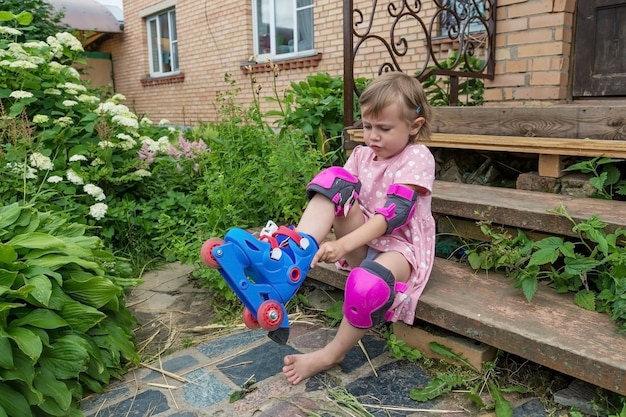 Una bambina veste i pattini a rotelle seduta sui gradini della sua casa di campagna.