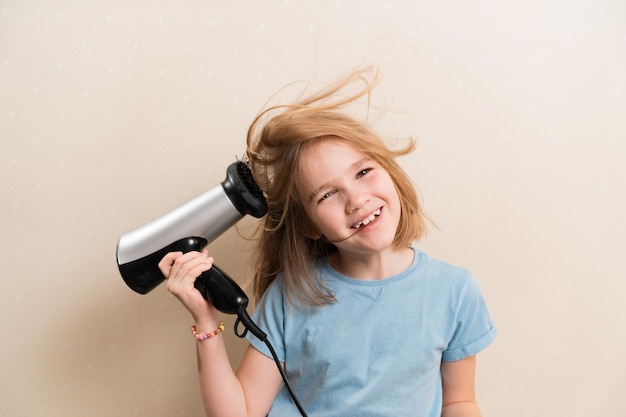 Little girl dries her hair with a hair dryer with a comb attachment