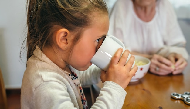 Маленькая девочка пьет чашку молока со своей бабушкой